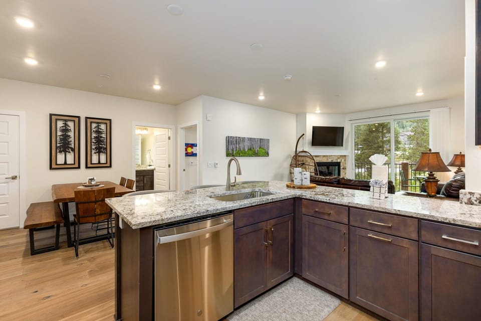 Modern open-concept kitchen with granite countertops, stainless steel appliances, and wood cabinets, leading into a living area with a fireplace and a view of an outdoor patio.