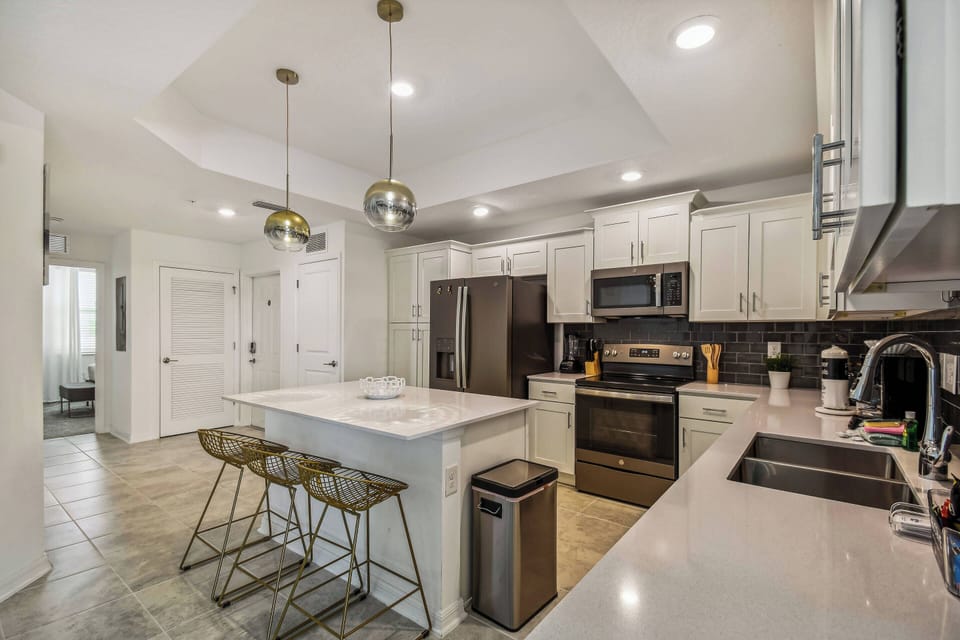 Experience a modern kitchen featuring stylish white cabinets and dark appliances. The spacious island, paired with chic gold bar stools, creates a perfect spot for casual dining, all in a warm and inviting atmosphere for your.