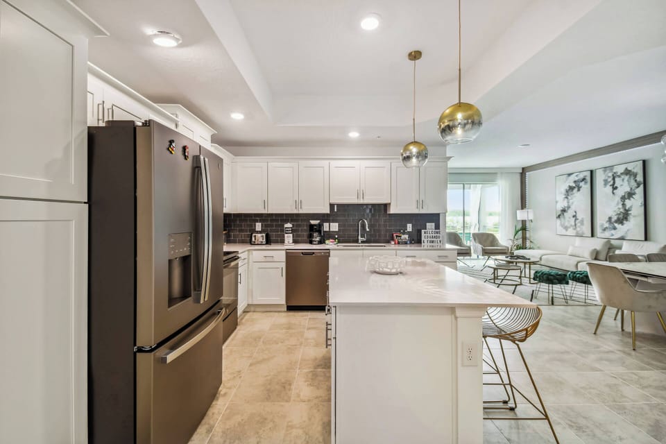 This stylish kitchen combines sleek white cabinetry with dark countertops for a contemporary look. Gold pendant lights add warmth, and the open layout connects beautifully to the dining area, making it perfect for gatherings.