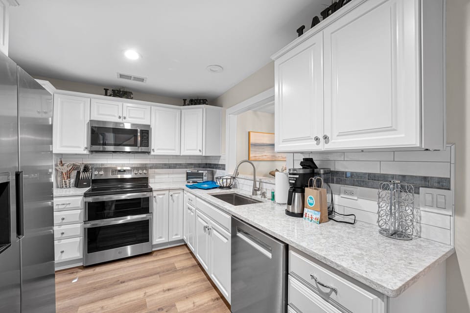 This bright, modern kitchen features sleek stainless steel appliances, crisp white cabinetry, and stylish tile accents