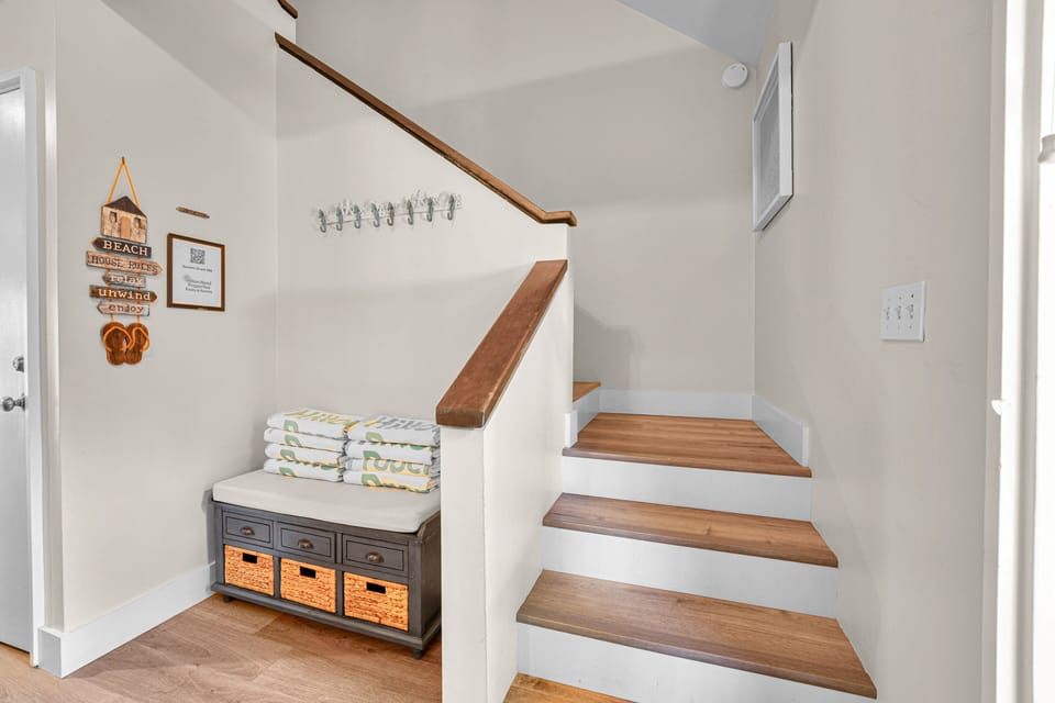 A welcoming entry nook featuring a cushioned bench with storage baskets, beach towels, and cheerful coastal decor
