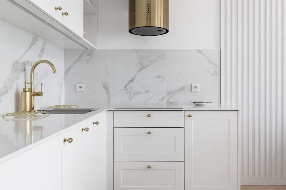 Compact kitchen with white cabinetry, gold handles, and marble-style backsplash.
