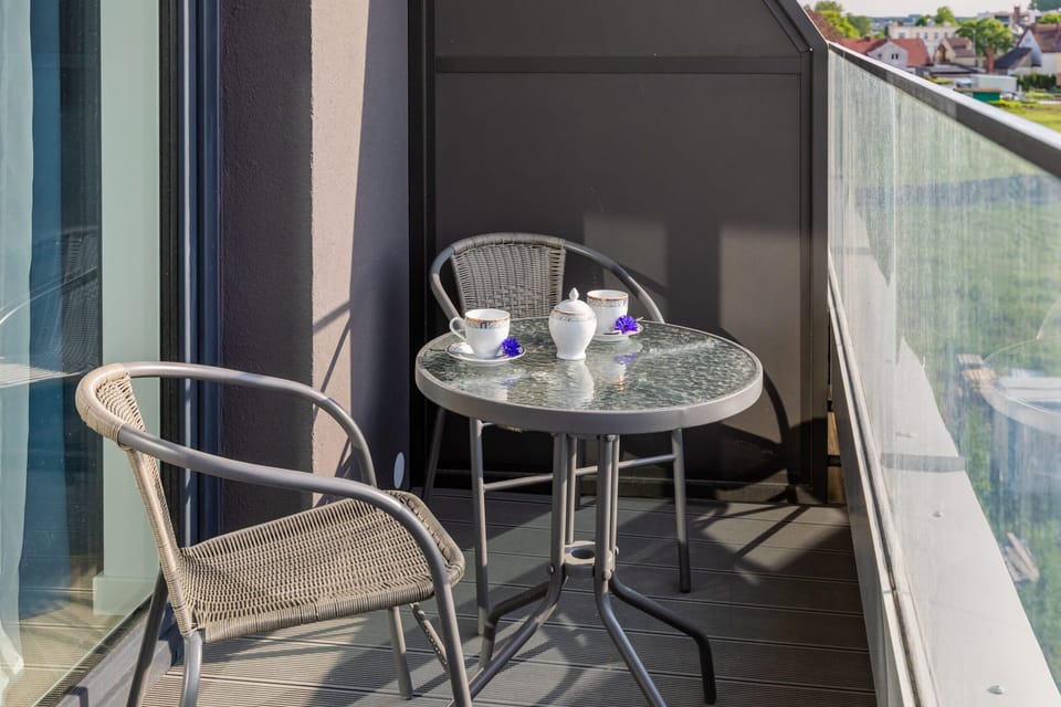 Balcony with a small table and chairs overlooking a green and peaceful view.
