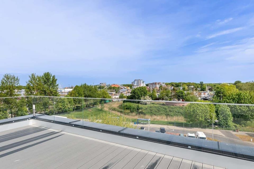 Rooftop view overlooking a residential area and green spaces under a clear sky.
