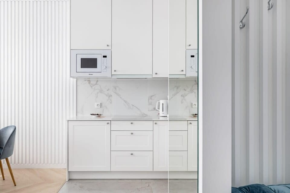 Compact kitchenette with white cabinets, a microwave, and a sleek marble backsplash.

