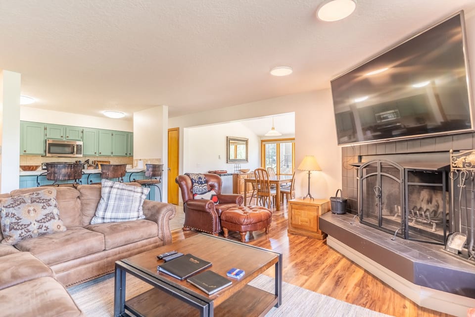 Spacious living area with large mounted flat screen TV, hardwood flooring, access to the private balcony, wood burning fireplace and ample seating.