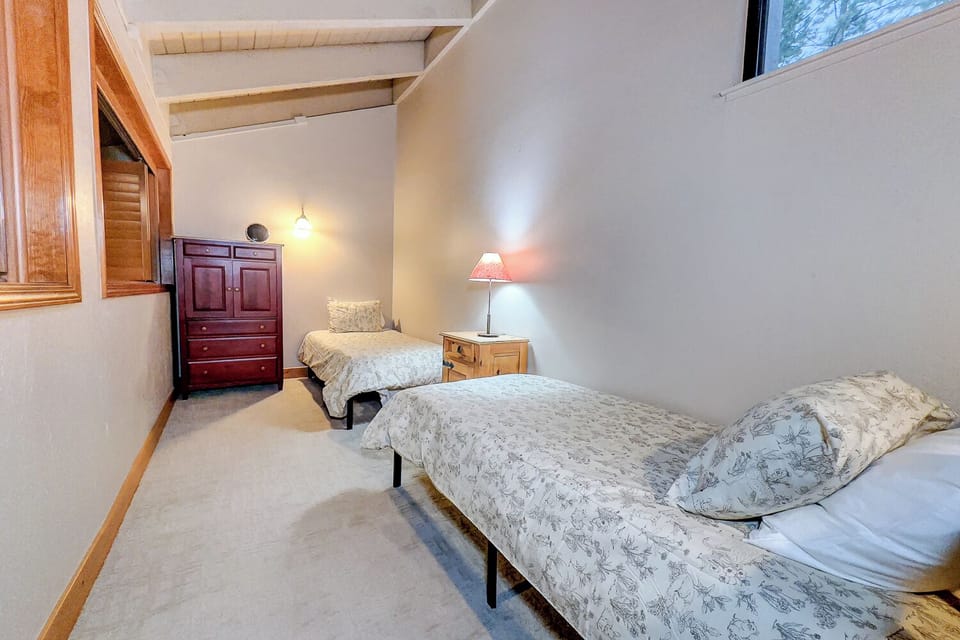 Rest peacefully in your cozy twin bedroom with rustic wood beams and warm lighting creating a charming retreat atmosphere.
