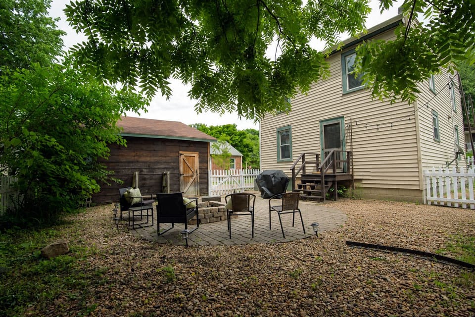 The leafy backyard provides outdoor seating, a fire pit, and a grill for guests to enjoy.