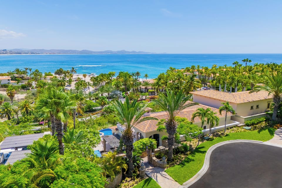 Aerial view of a beachfront property with lush tropical landscaping, private pool, and direct access to pristine turquoise waters and sandy shores.