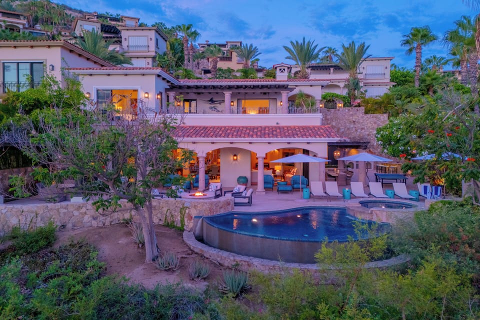 Stunning hillside villa nestled among palms and lush gardens, featuring private pool, multiple terraces, and dramatic views at twilight.
