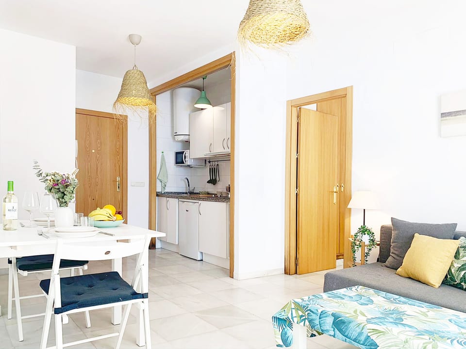 Comfortable living-dining room with access to the kitchen, a table for two, a sofa bed, a microwave, a stove, and a refrigerator