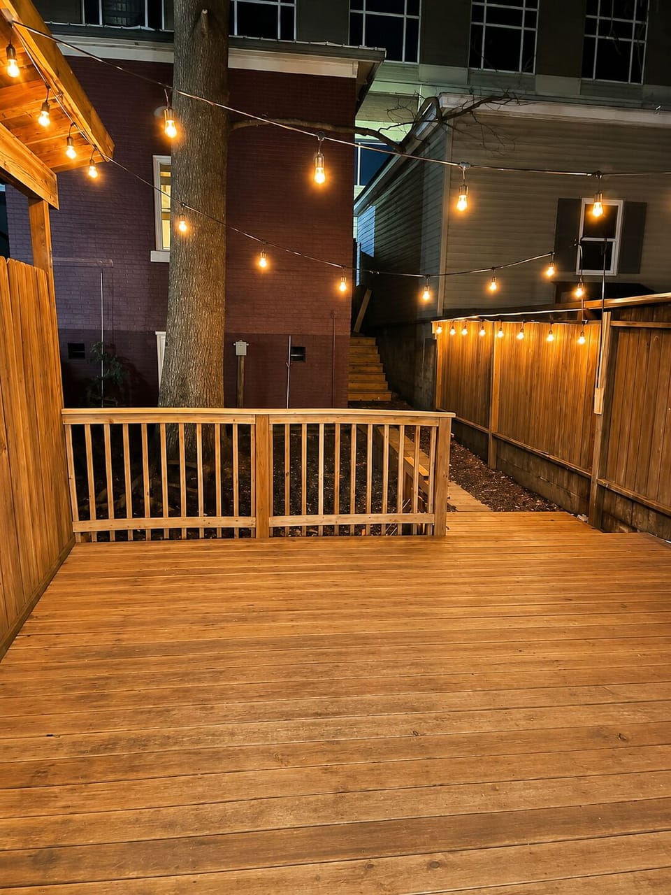 The private wood deck is enclosed by fencing and softly lit with overhead string lights.