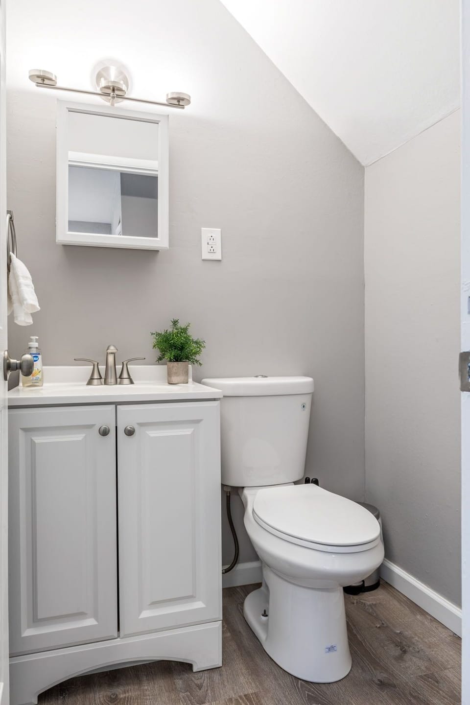Compact powder room with a white vanity, toilet, and sloped ceiling.