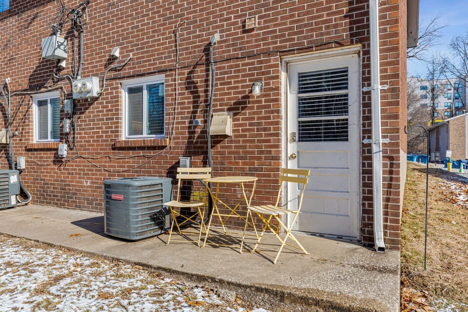 Small concrete patio at the rear door with a yellow bistro table and two chairs.