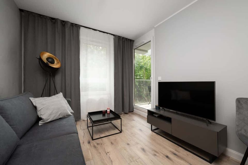 Cozy living room with a gray sofa, TV, and large window overlooking greenery.
