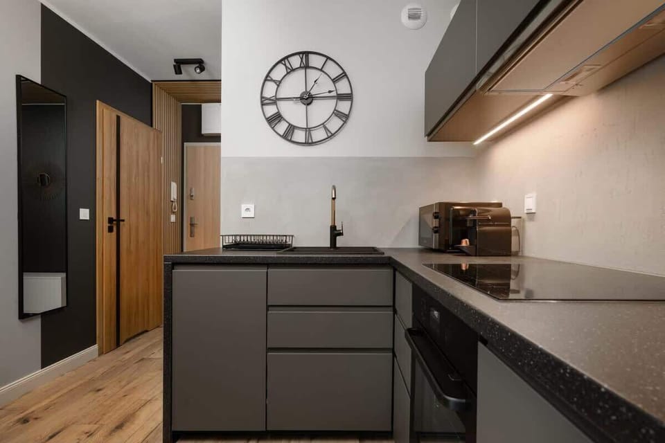 Sleek kitchenette with black countertops, a wall clock, and stylish decor.
