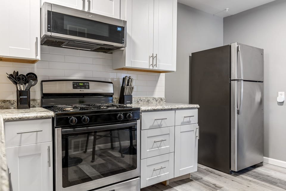 White shaker cabinetry and speckled counters surround a black gas range, over-the-range microwave, and stainless-steel-finish refrigerator.