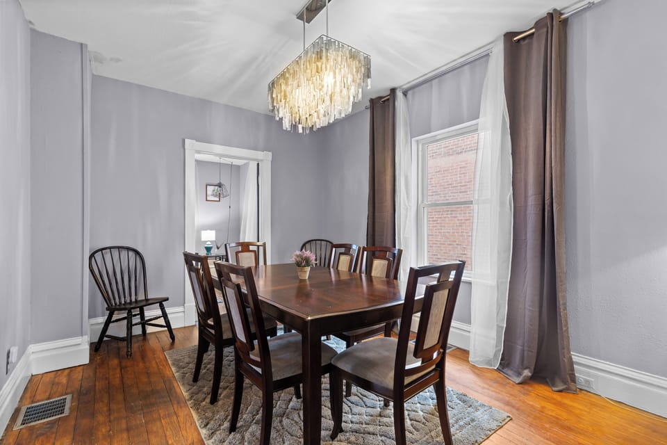 Opposite dining-room angle centered on the eight-seat table, chandelier, windows, and living-room doorway.