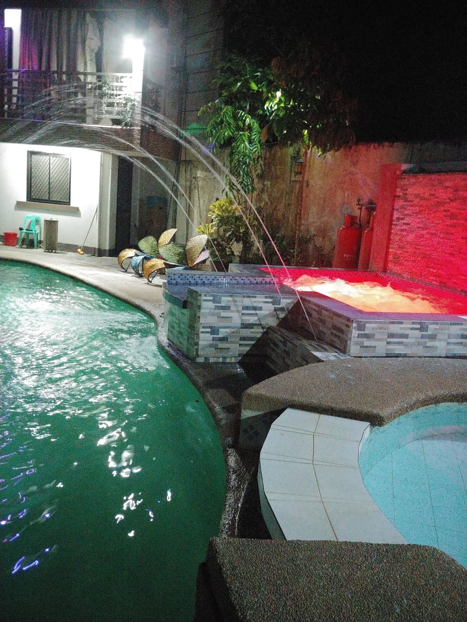 Hot tub at night with red illumination. Pool to left, paddling pool in front