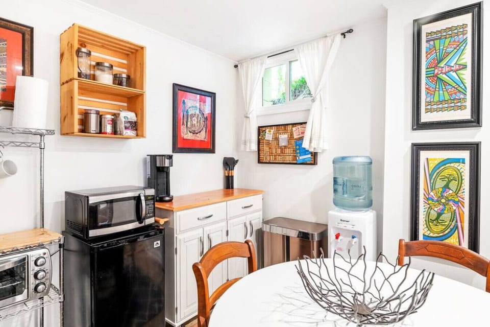 This kitchenette area has a small dining table, trashcan, water cooler, coffee maker, mini fridge, microwave, toaster oven as well as a hot plate and pots and pans.