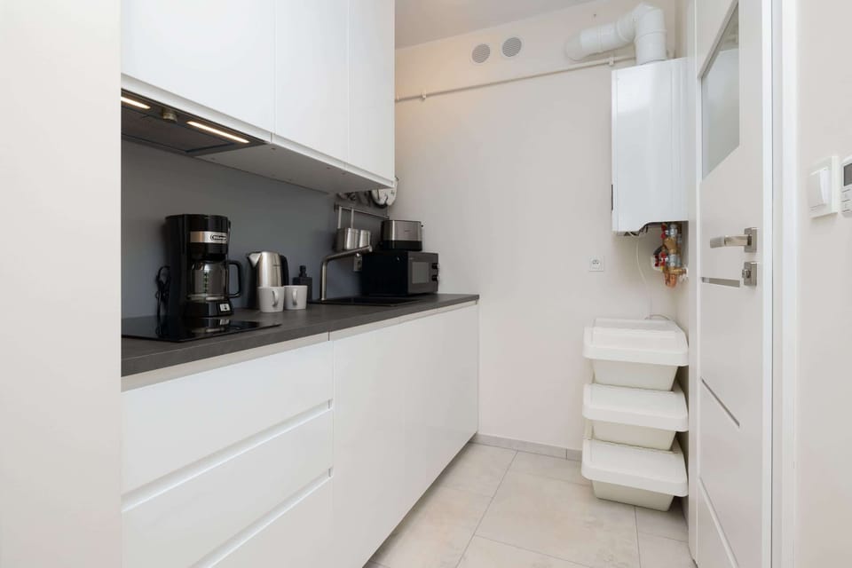 A modern kitchen with a coffee machine, kettle, and white cabinets.