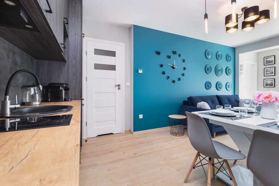 A modern kitchenette with sleek gray cabinets, a black countertop, and a dining table nearby. The turquoise accent wall adds a splash of color, enhancing the stylish and functional space.