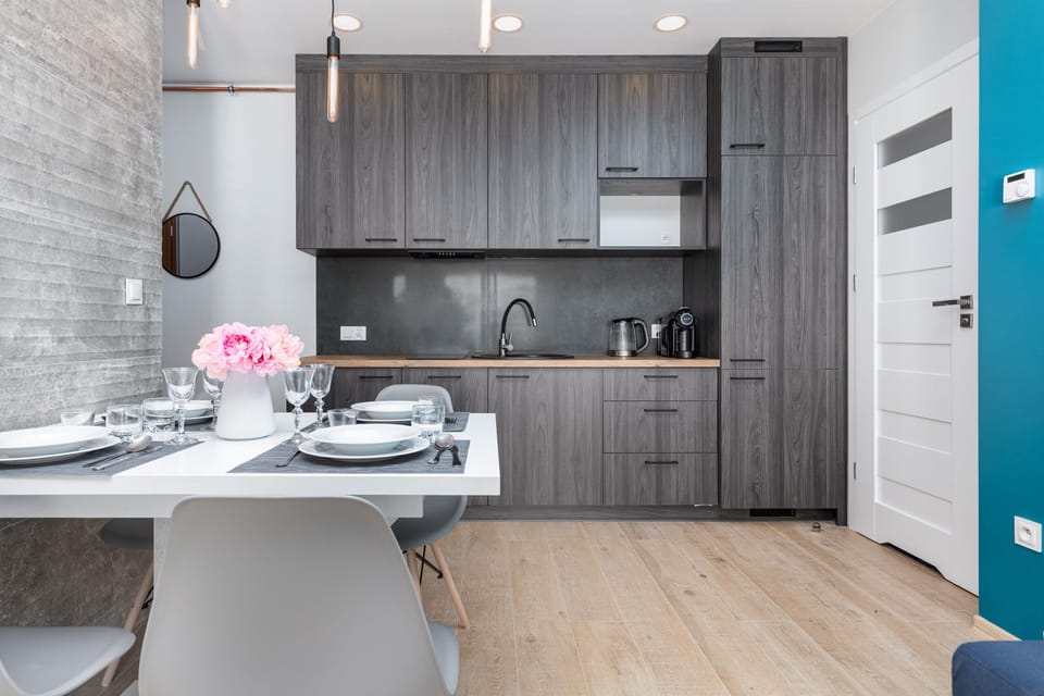 A compact modern kitchen with dark wood cabinets and a small counter with a pink floral centerpiece. The kitchen has modern fixtures.