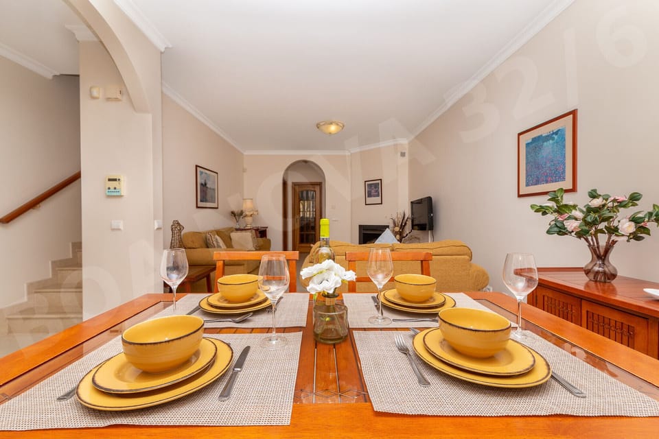 Open-plan dining area at Boa Nova 32/6 with table beautifully set with yellow crockery and wine glasses, flowing through to the comfortable living room in this spacious Vilamoura holiday apartment