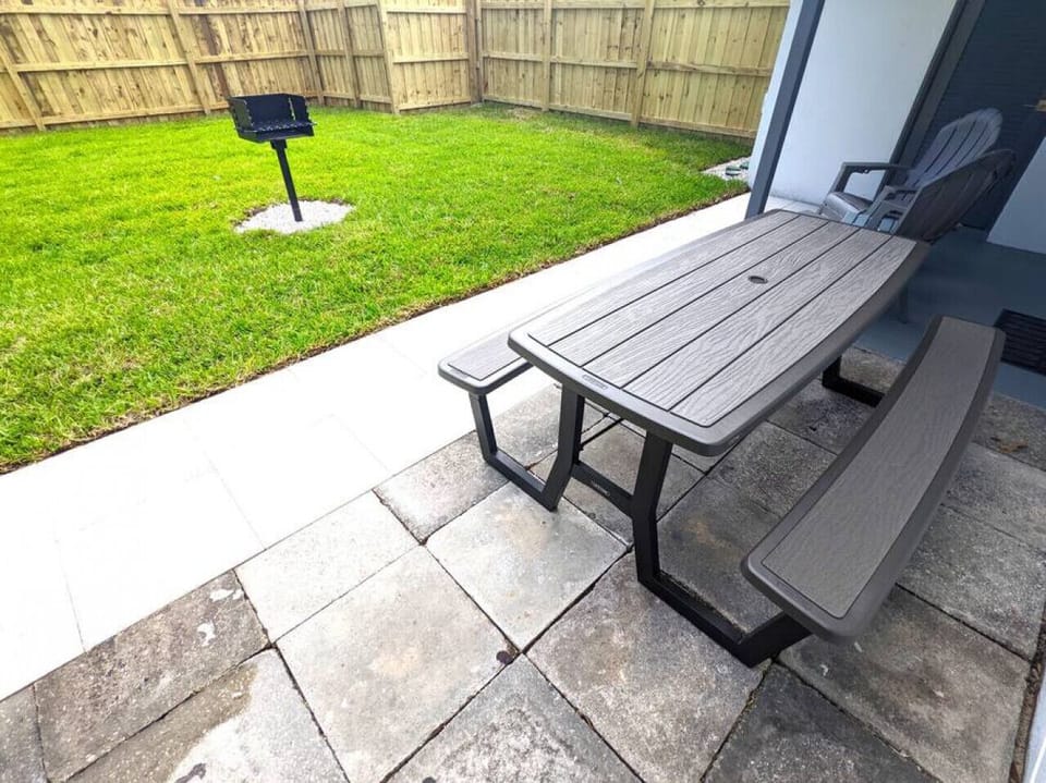 Another view of the lush green landscaped, private, fenced-in backyard with a large partially covered patio, outdoor dining area, Adirondack chairs, outdoor patio lighting, and grill.