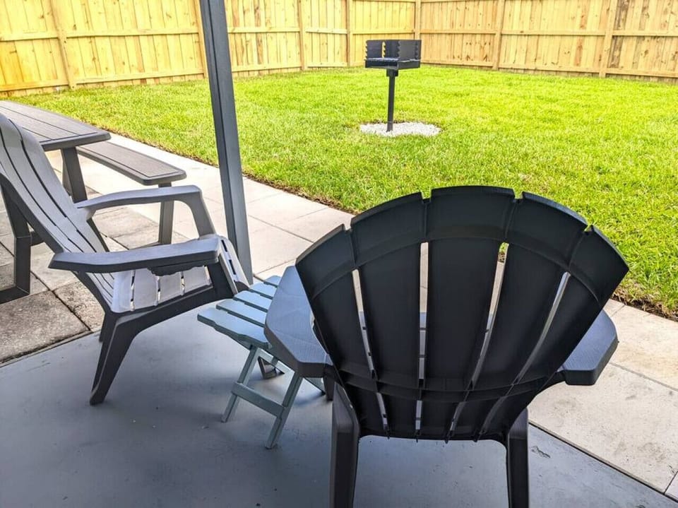 Lush green landscaped, private, fenced-in backyard with a large partially covered patio, outdoor dining area, Adirondack chairs, outdoor patio lighting, and grill.