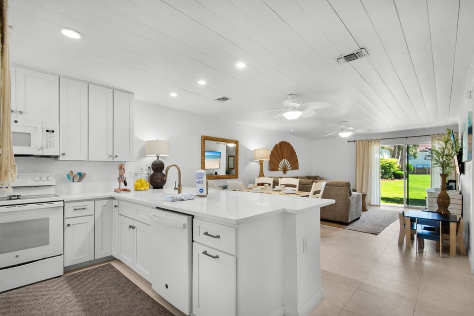 Your open-concept retreat features a bright coastal kitchen flowing into a relaxed living space, with views of lush greenery just outside your door.