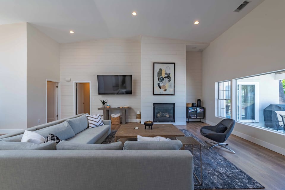 Sink into the plush sectional and unwind by the fireplace in this airy living room, where vaulted ceilings and modern touches create a serene retreat for your relaxation.