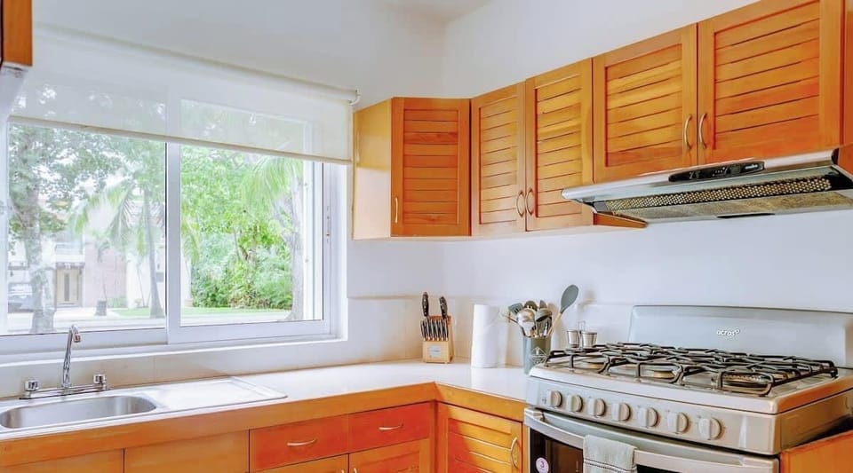 Bright kitchen with wooden cabinets and a large window overlooking greenery.