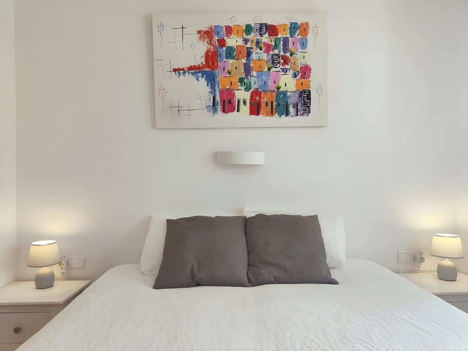 The bedroom features a comfortable queen-sized bed. The room is bathed in soft natural light, creating a relaxing and inviting atmosphere.  Nightstands with lamps are located on either side of the bed, providing ambient light for reading or evening relaxa