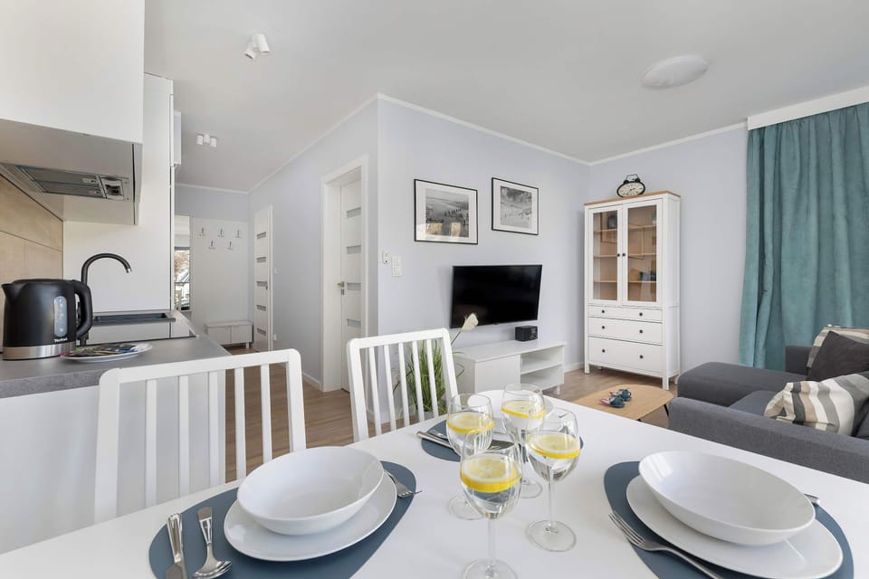 A dining table set with plates, glasses, and simple decor. White chairs surround the table, creating a clean aesthetic. The setup looks ready for a meal.