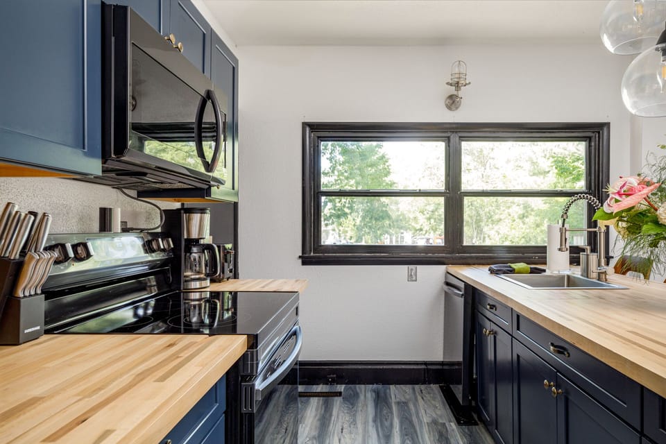 Stylish kitchen w/ butcher block counters, dark cabinets & wide window over the sink.