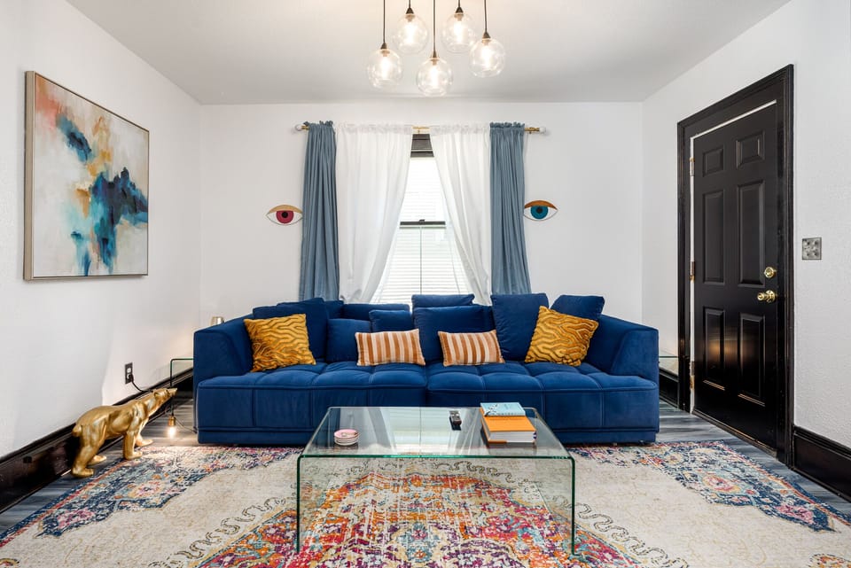 Bright living room w/ bold blue sofa, colorful rug & tall windows bringing in natural light.