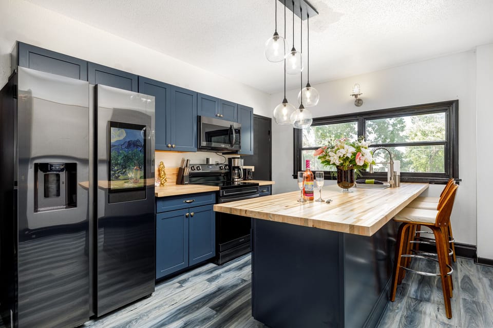 Spacious kitchen w/ large island, stainless steel fridge & window views for easy meal prep.