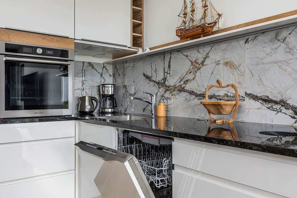 A modern kitchenette with wooden cabinets and a marble countertop, equipped with a coffee maker and kettle.