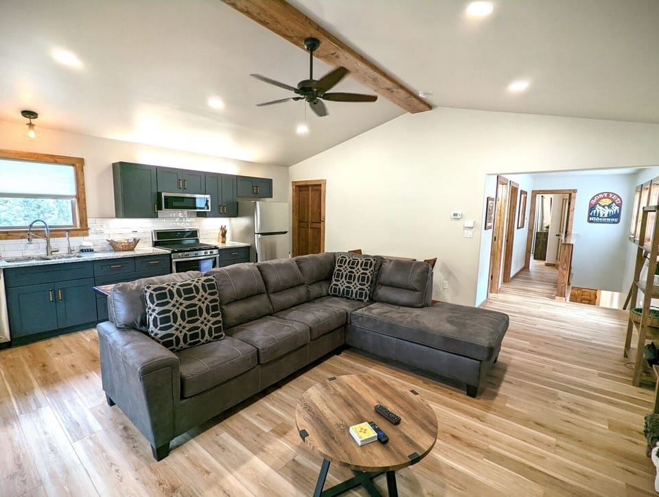 Step into your cozy open-concept retreat with vaulted ceilings, modern kitchen, and plush sectional seating—where warm wood tones and natural light create a welcoming home away from home.