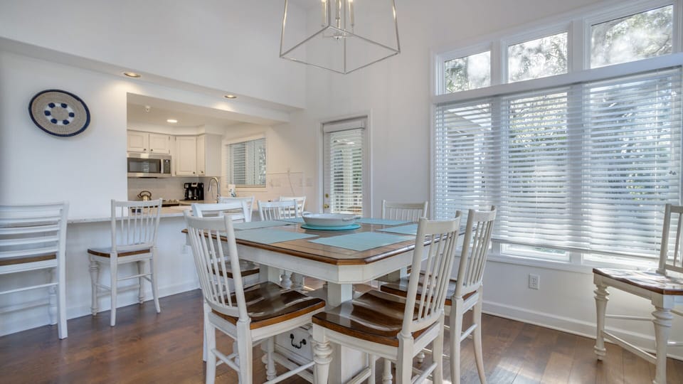 A spacious table comfortably seats family and friends, while natural light pours in from multiple angles, creating an inviting, open feel.