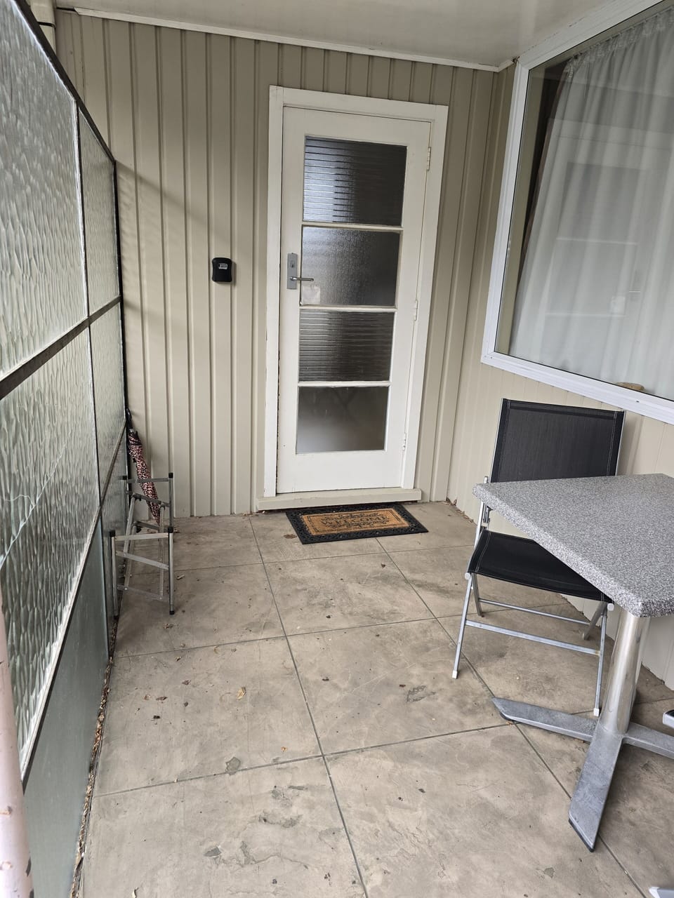Sheltered entrance to studio next to glass partition, outdoor seating on patio
