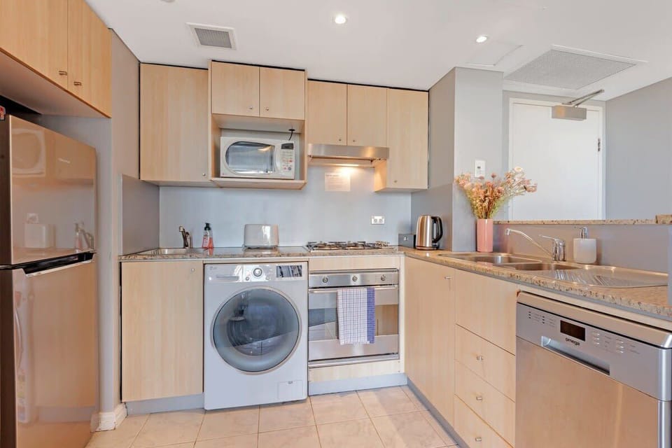 Fully equipped kitchen with cooktop, oven, microwave, dishwasher, washing machine, and ample cabinetry.
