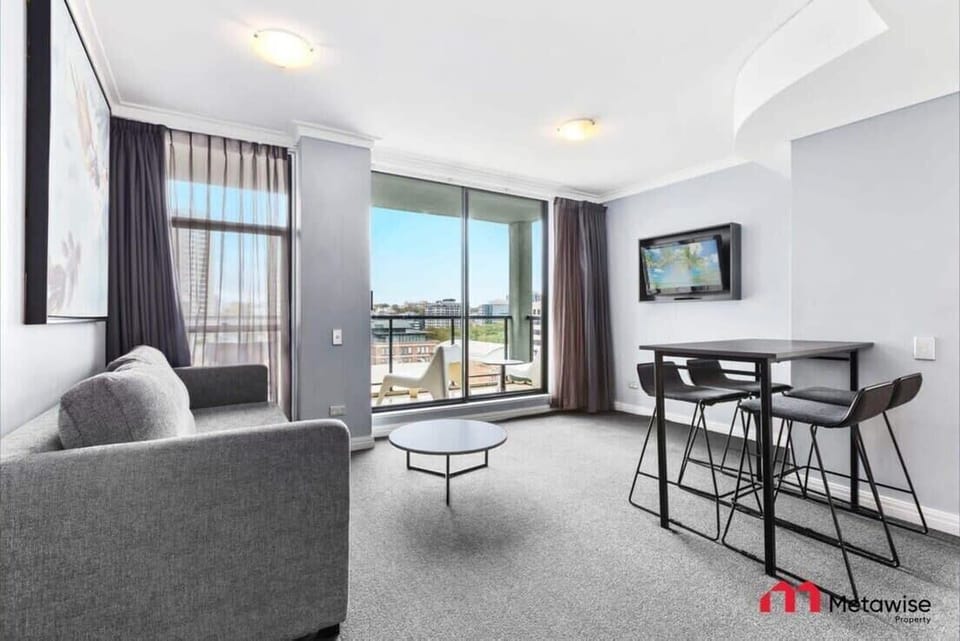 Living area with sofa seating, dining space, wall-mounted TV, and city views. (Includes sofa bed for additional guests.)