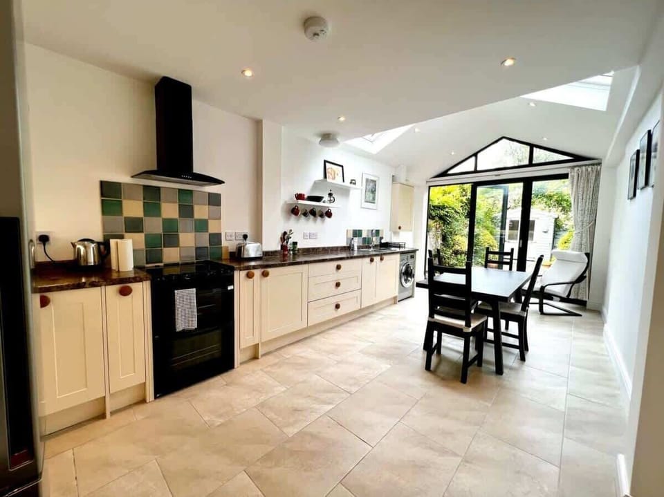 A spacious, sun-filled kitchen and dining area featuring sleek appliances, tiled flooring, and large glass doors that open directly onto the garden.