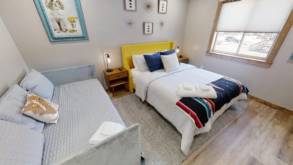 Unwind in your cozy bedroom featuring a cheerful yellow headboard, soft textured linens, and a reading nook by the sofa—natural light floods in from skylights above.