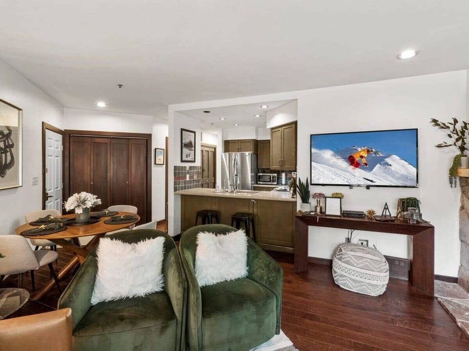 This view from the living area highlights the plush armchairs and large, flat-screen TV as well as the close proximity of the dining and kitchen areas that makes for easy movement and socializing between the spaces.