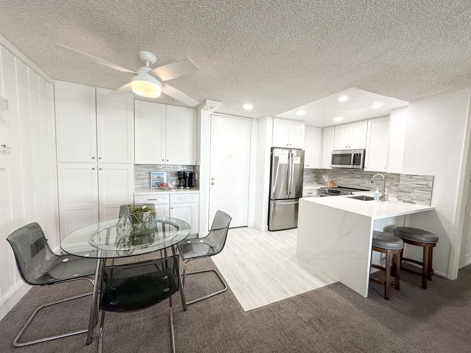 Glass dining table with seating for four, plus two additional barstools at the kitchen counter—ideal for kids or casual snacks.