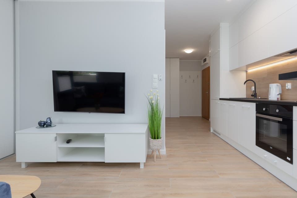 A sleek entertainment area with a mounted flat-screen TV, a white console beneath, and an open kitchen to the side.