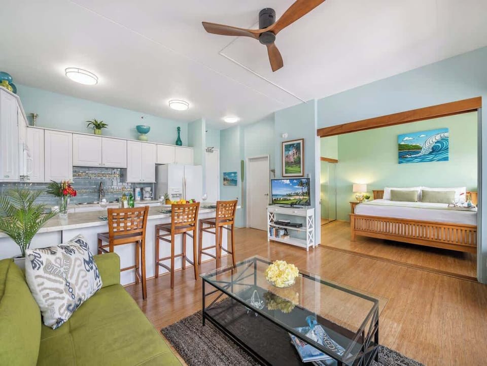 Living room with ceiling fan, smart TV with cable box, kitchen and counter top with 3 barstools